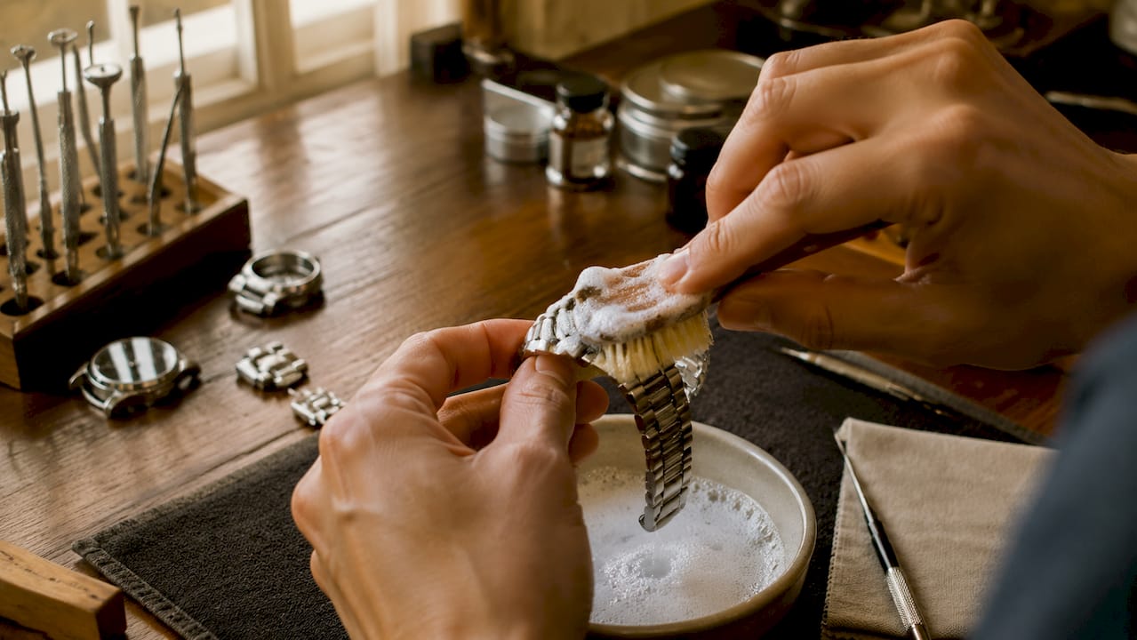 Hands applying foam spray to metal watch bracelet