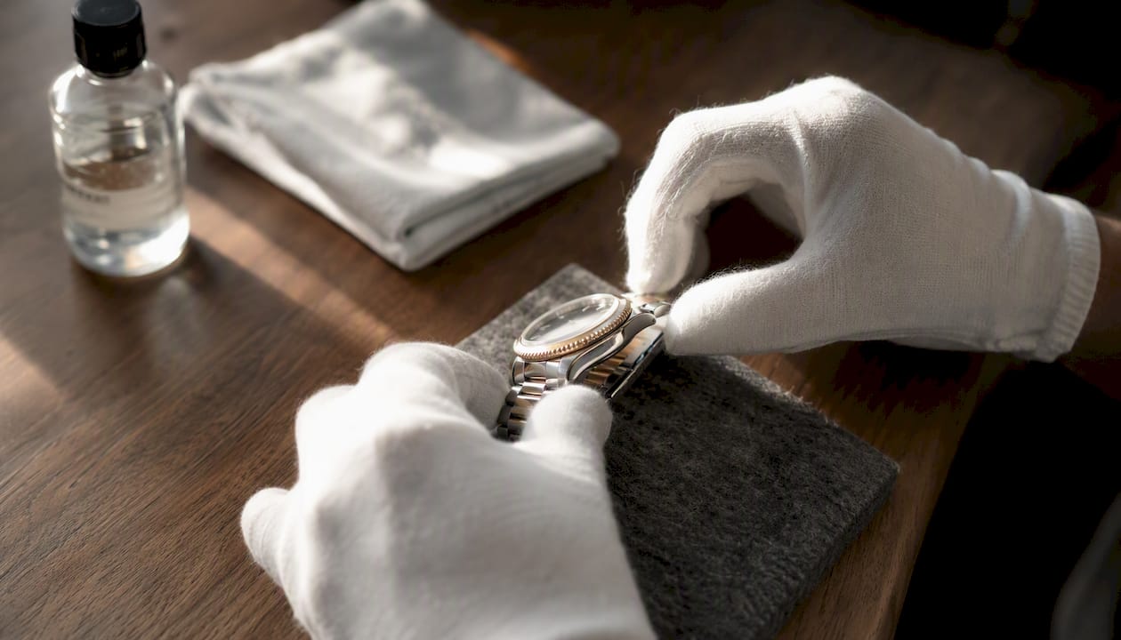 Hands with cotton gloves handling luxury watch on microfiber pad