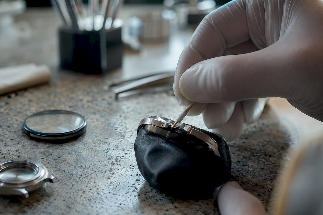 Hand sliding cloth-wrapped toothpick into watch crown gap