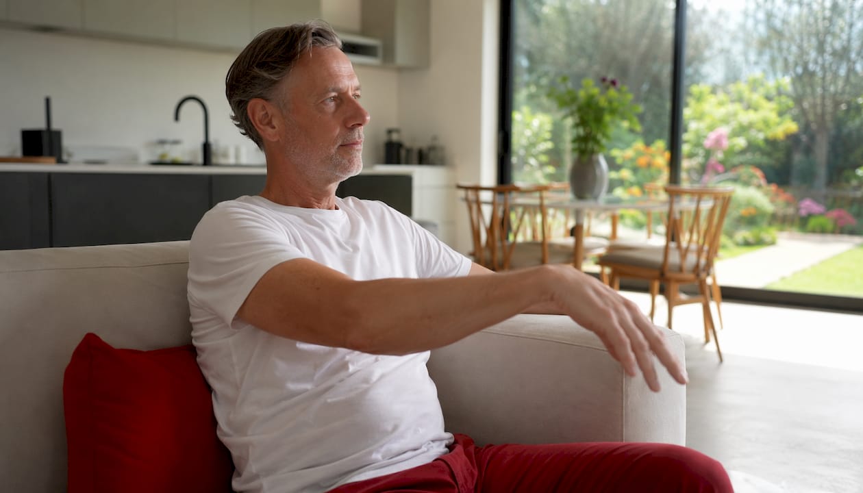 Een man doet thuis schouderoefeningen waarbij hij zijn armen heen en weer zwaait.