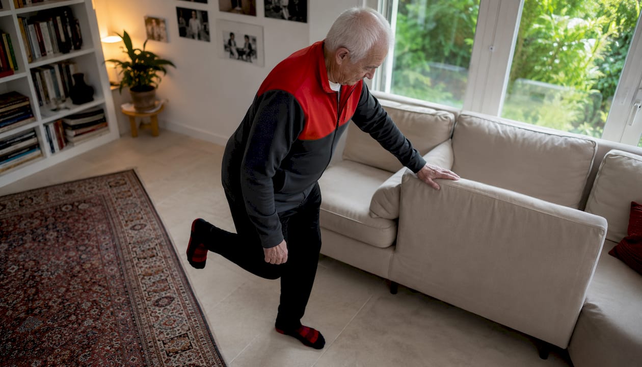 Een oudere man werkt thuis aan zijn balans door speciale oefeningen te doen.