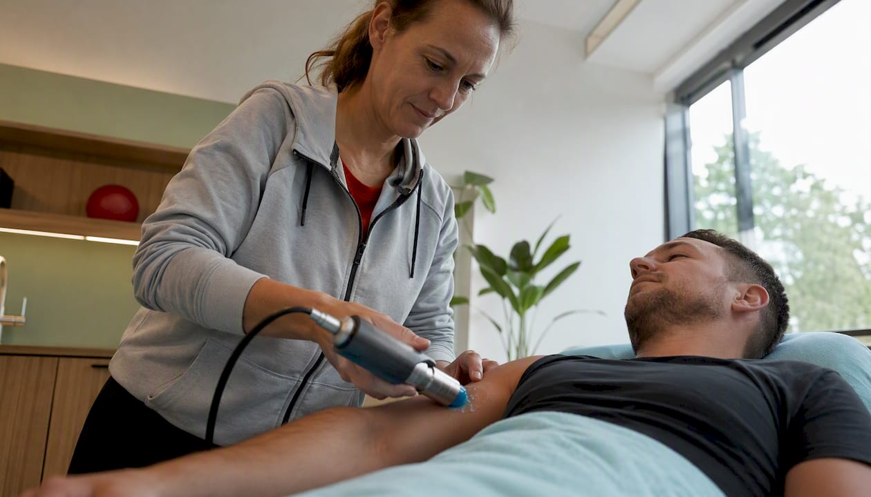 Een behandelaar brengt met zijn handen shockwave-therapie aan op de arm.