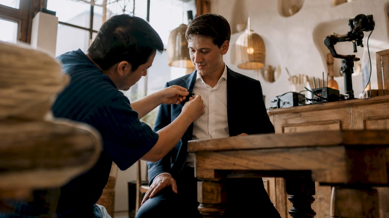 Videographer adjusting lapel microphone on groom indoors