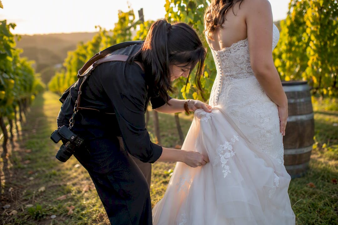 Photographer adjusting bride’s bustle outdoors