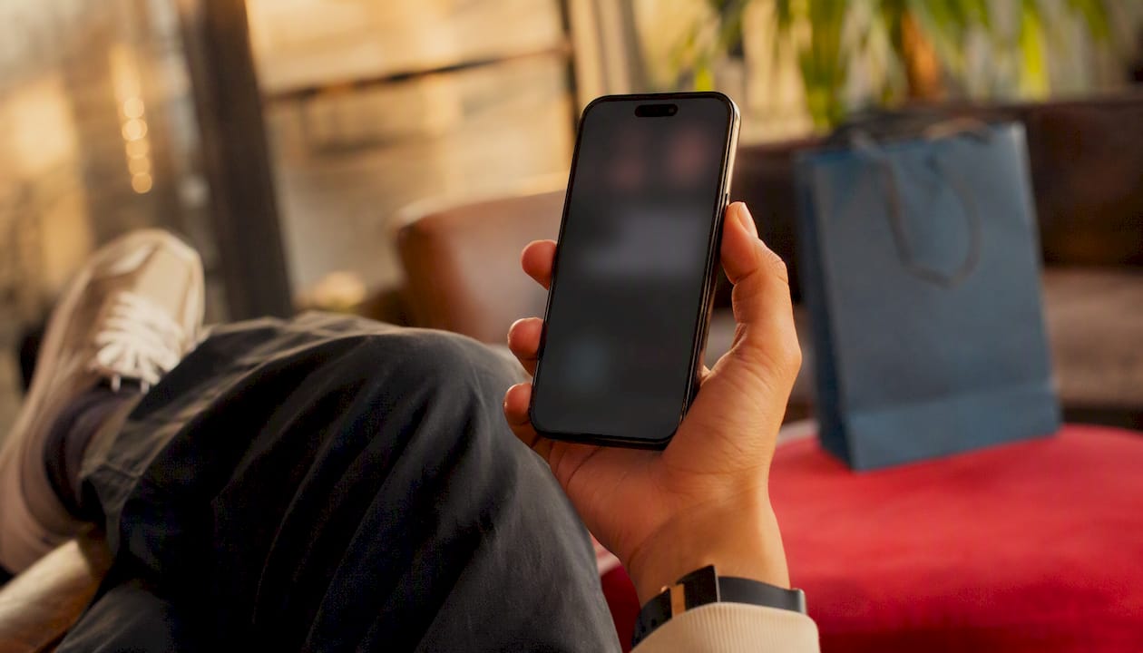 Hand holding phone near trainers and shopping bag