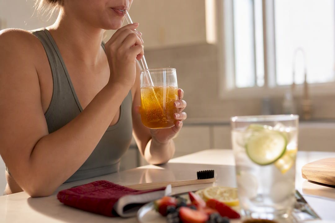 Person sipping kombucha with straw to protect teeth