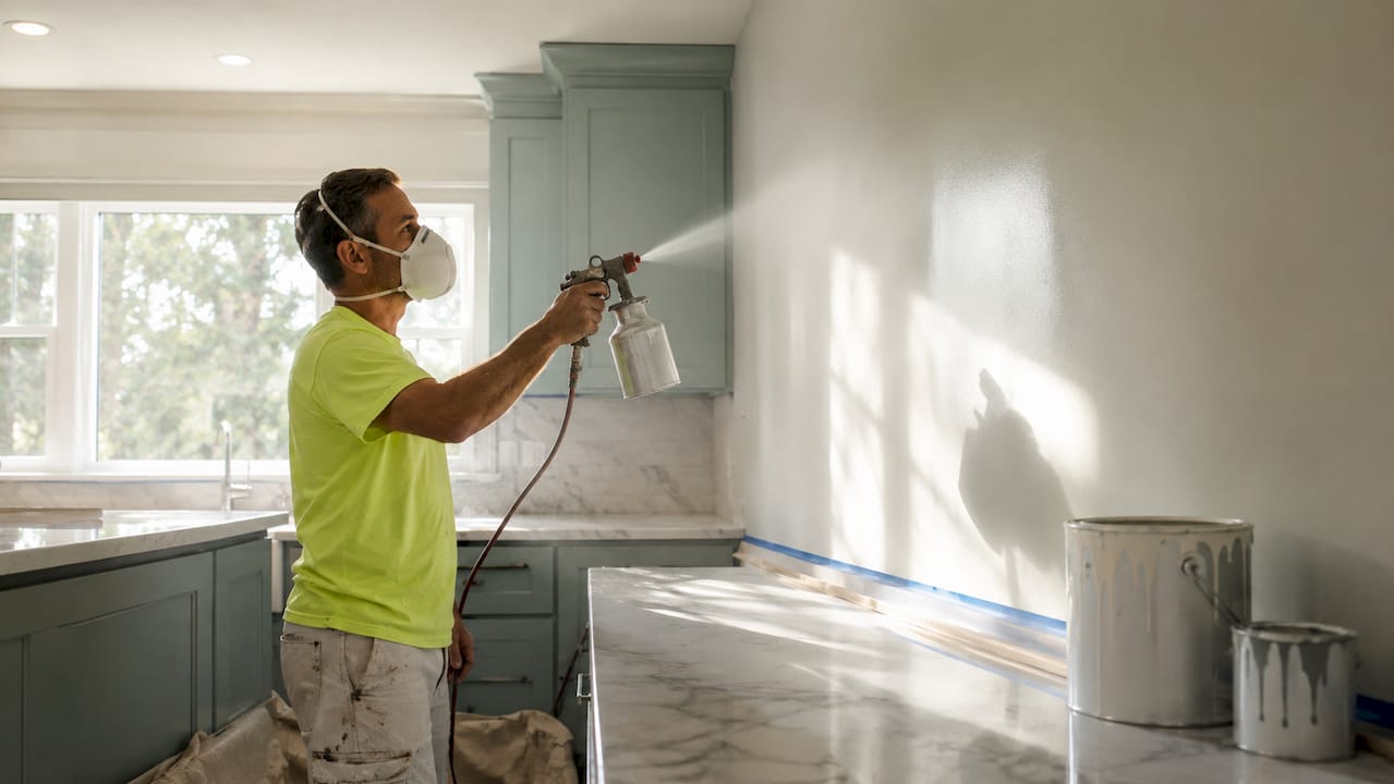 Contractor spraying paint on a wall indoors