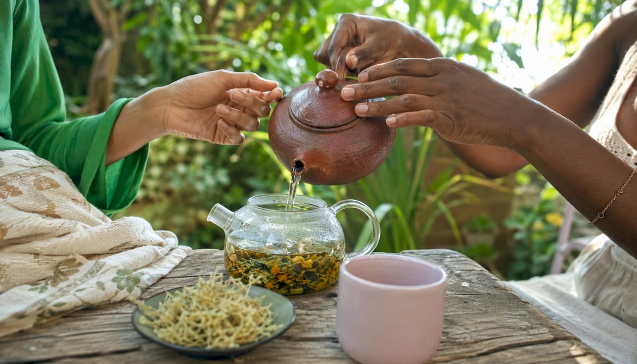 Hands pouring hot water over alkaline herbs in teapot