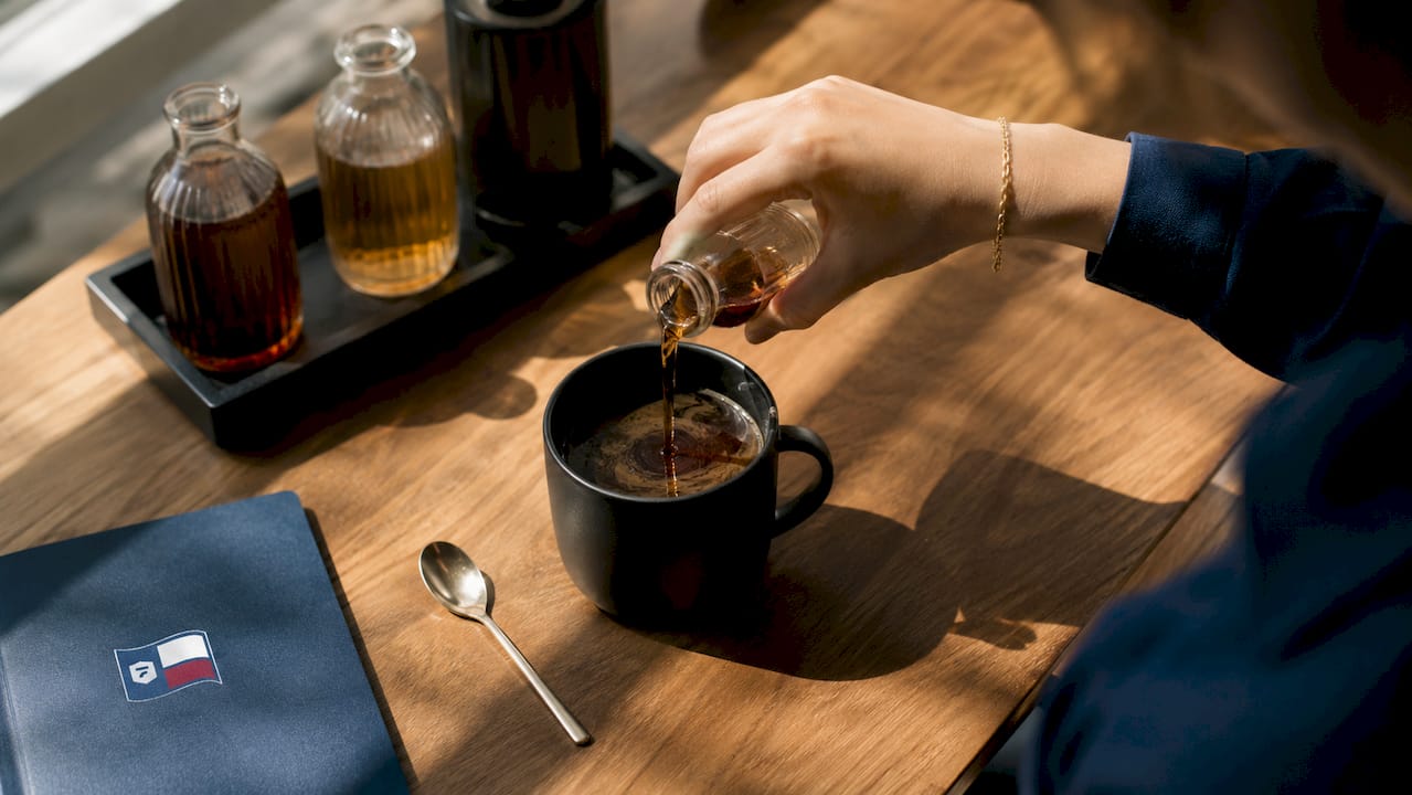 Hands measuring syrup over coffee mug close-up