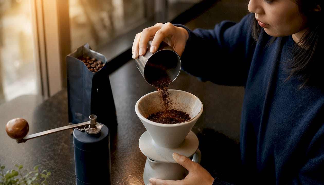 Hands pouring fresh ground coffee into pour-over brewer