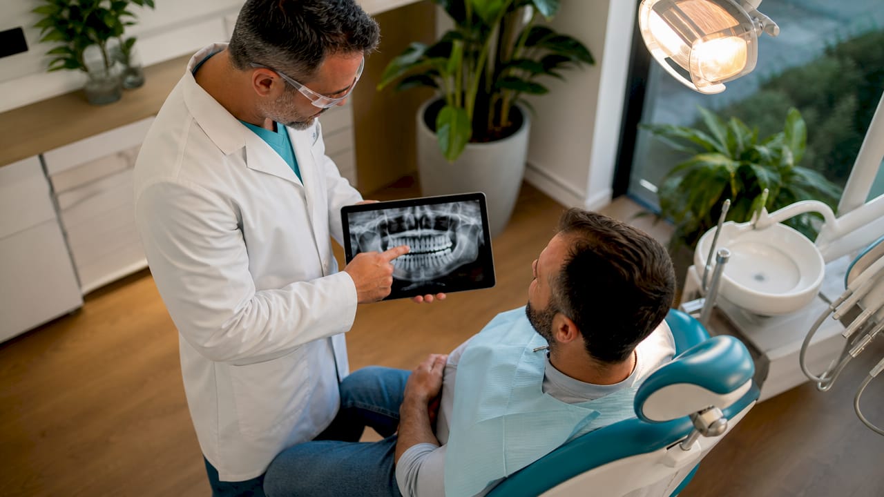 Il dentista illustra la radiografia al paziente seduto sulla poltrona.