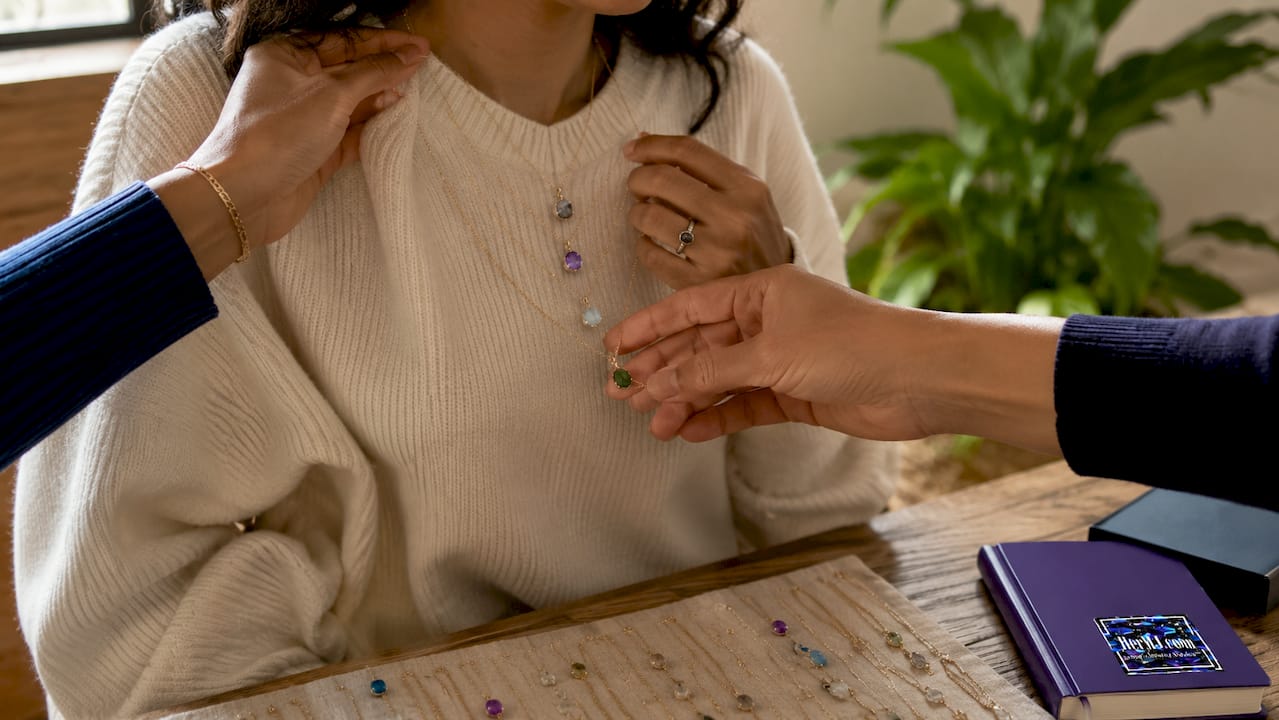 How to Pair Gemstone Pendants with Casual Necklines Close-up hands layering gemstone pendant necklaces on casual top