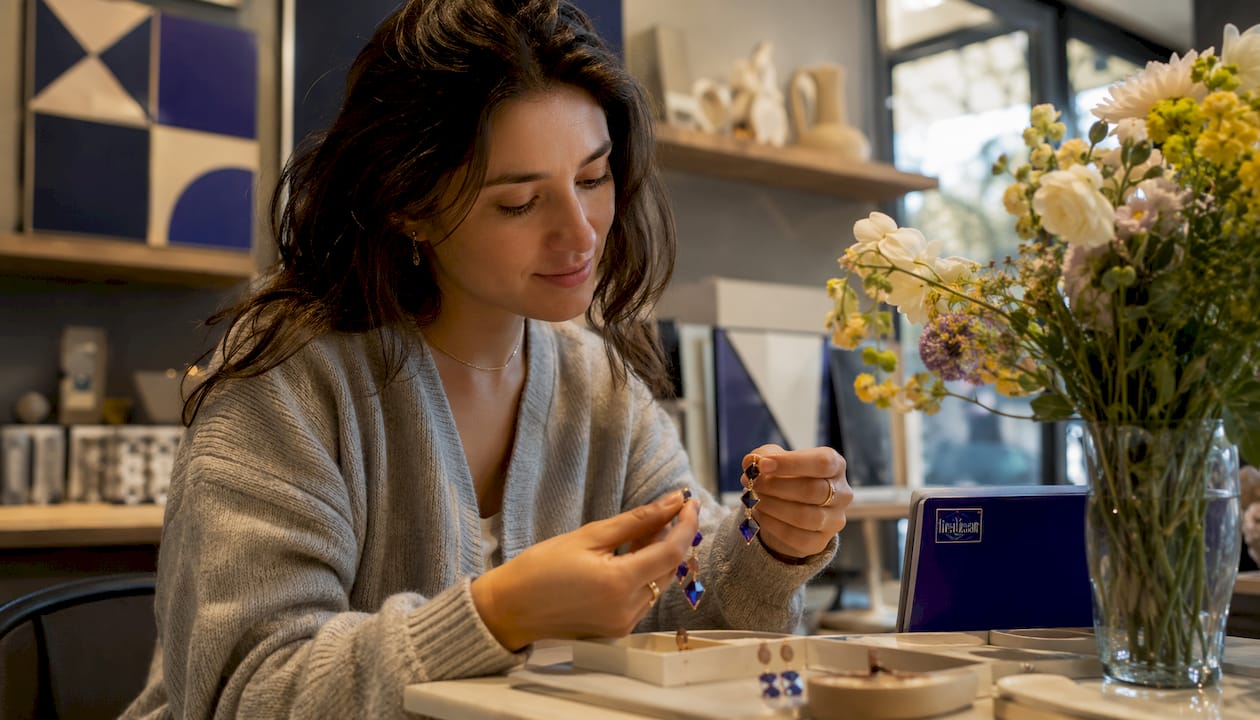 What Is Asymmetrical Jewelry Design? A Style Guide Woman examining asymmetrical earrings by window light
