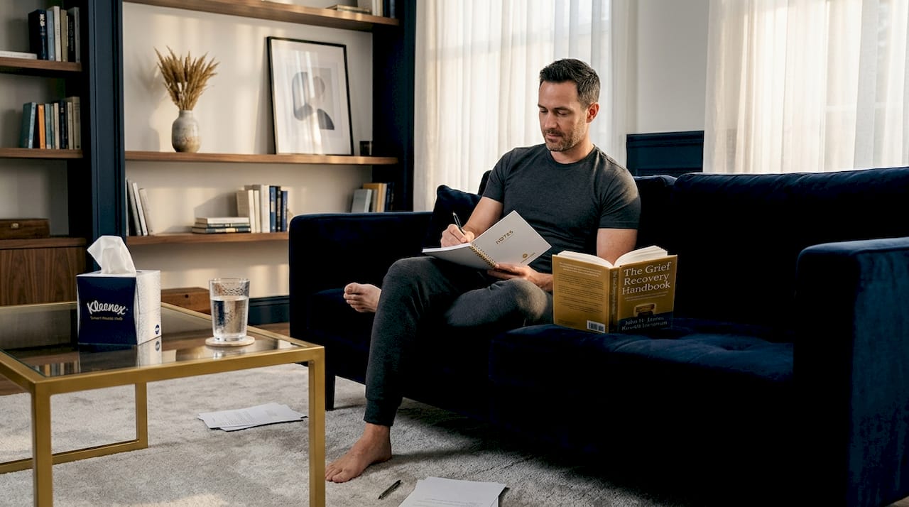 Man journaling with grief recovery book nearby