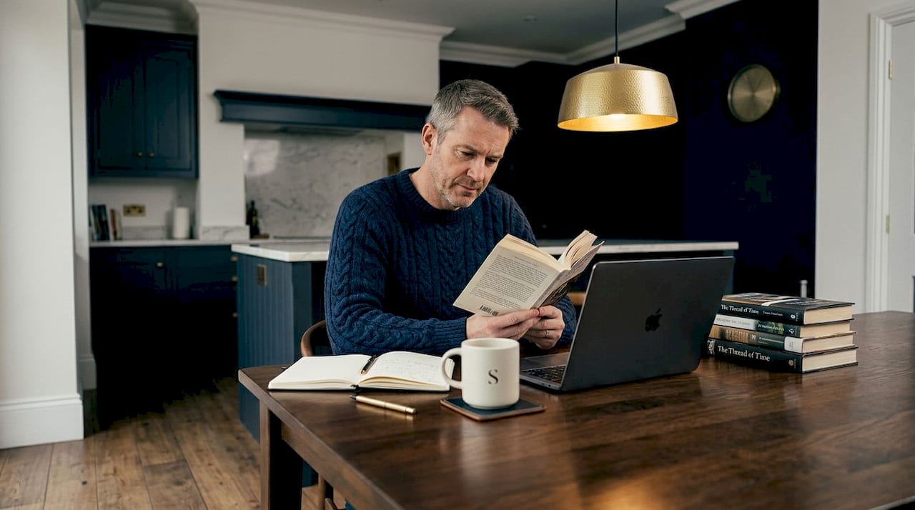 Man reading paperback at kitchen table break