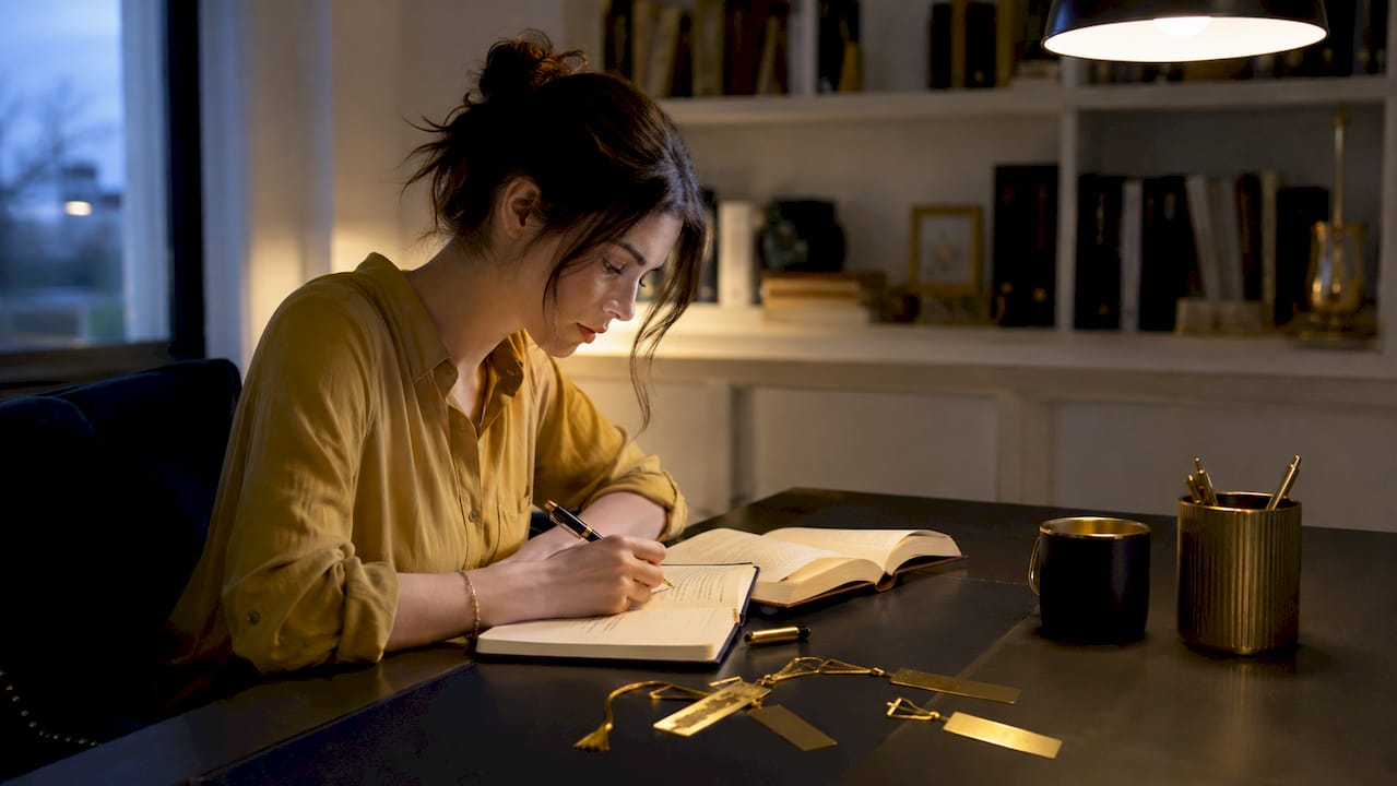 Hands writing in reading journal at wooden desk