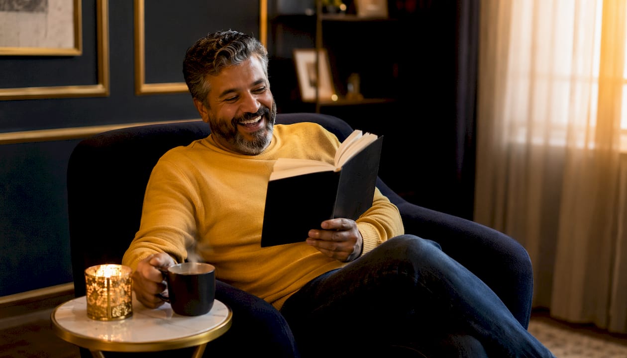Man laughing while reading humor book at desk