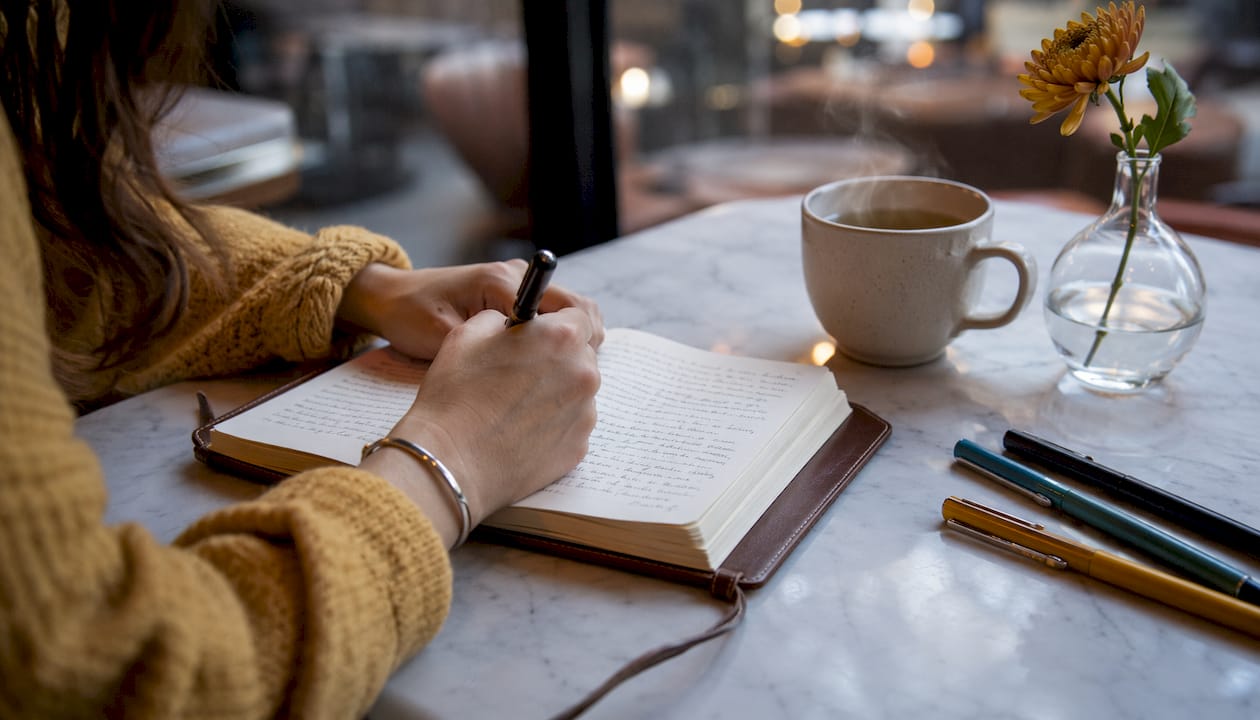 Hands writing in journal near window