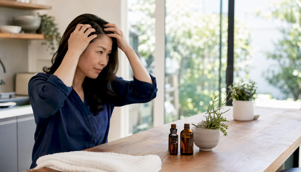 Woman applying rosemary oil to scalp in bathroom