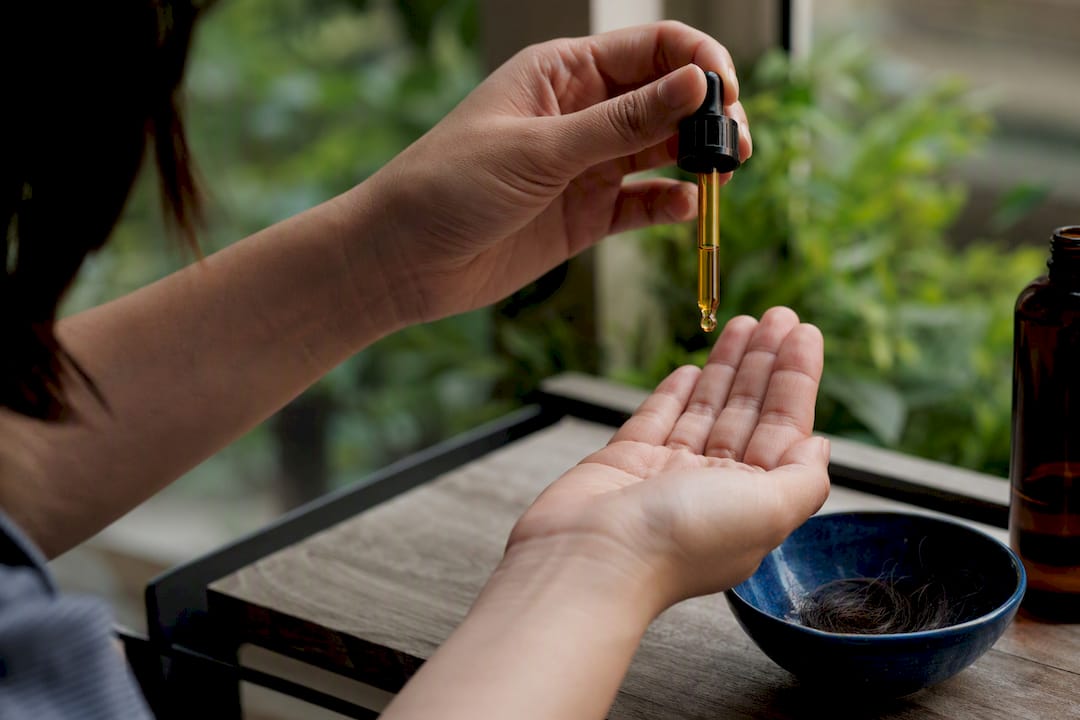 Hand measuring hair oil drops with dropper