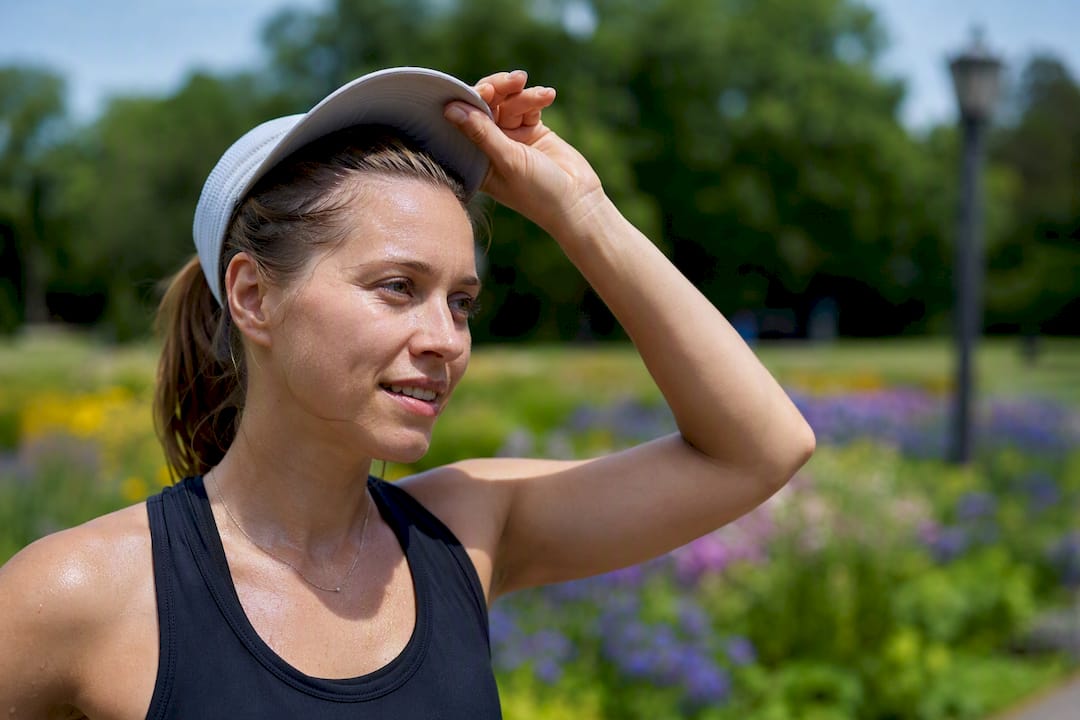 Woman lifting hat showing sweaty scalp