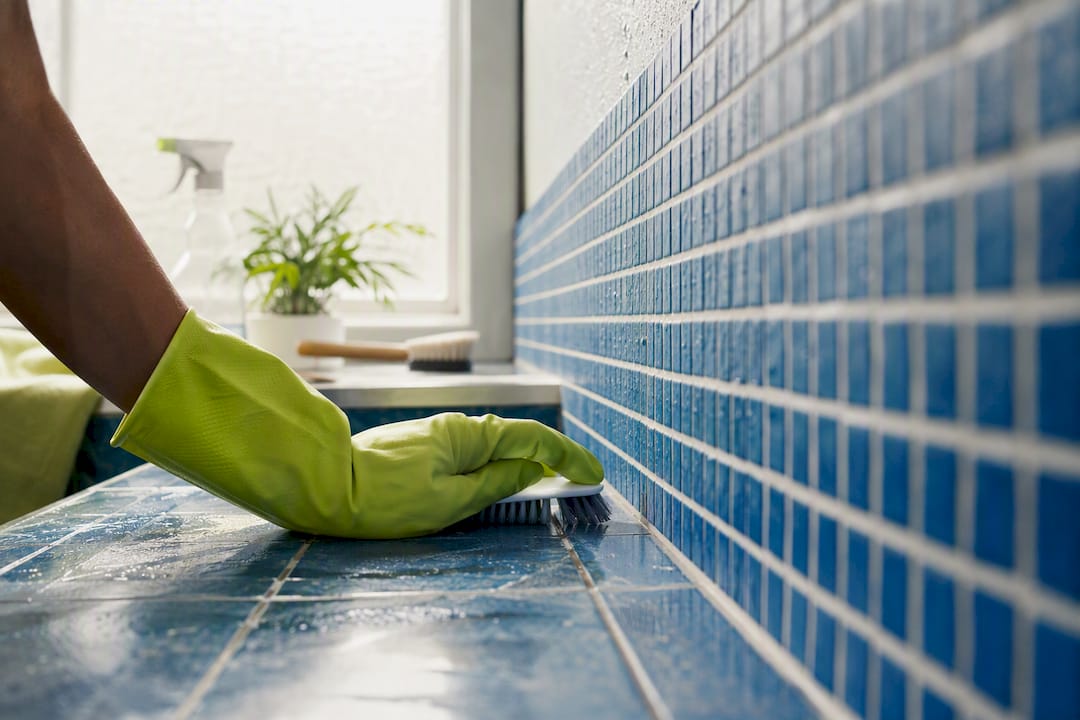 Gloved hand scrubbing grout in rental bathroom