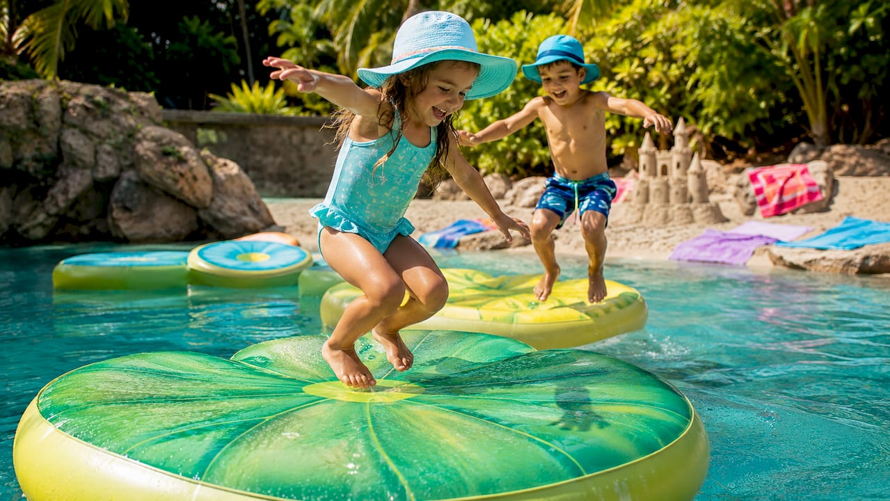 Kids playing on floating lily pad inflatables near sandbar