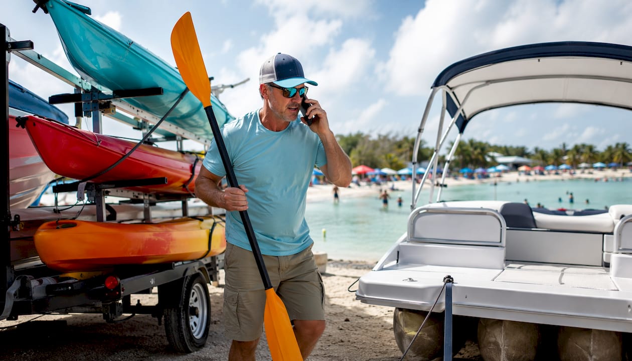 Man unloading kayaks beside pontoon boat at beach