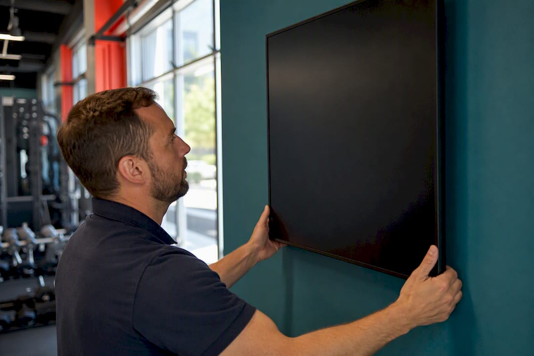Hands adjusting digital signage screen mount in gym