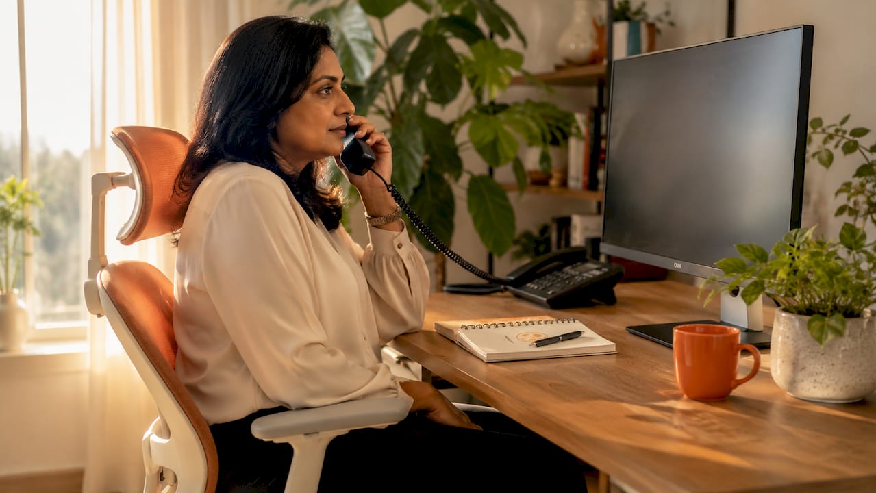 Woman using phone and laptop in small office