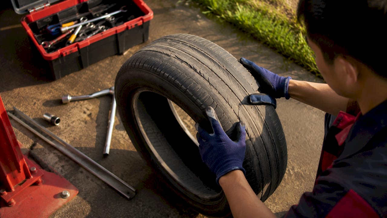 Hands inspecting worn car tire in garage