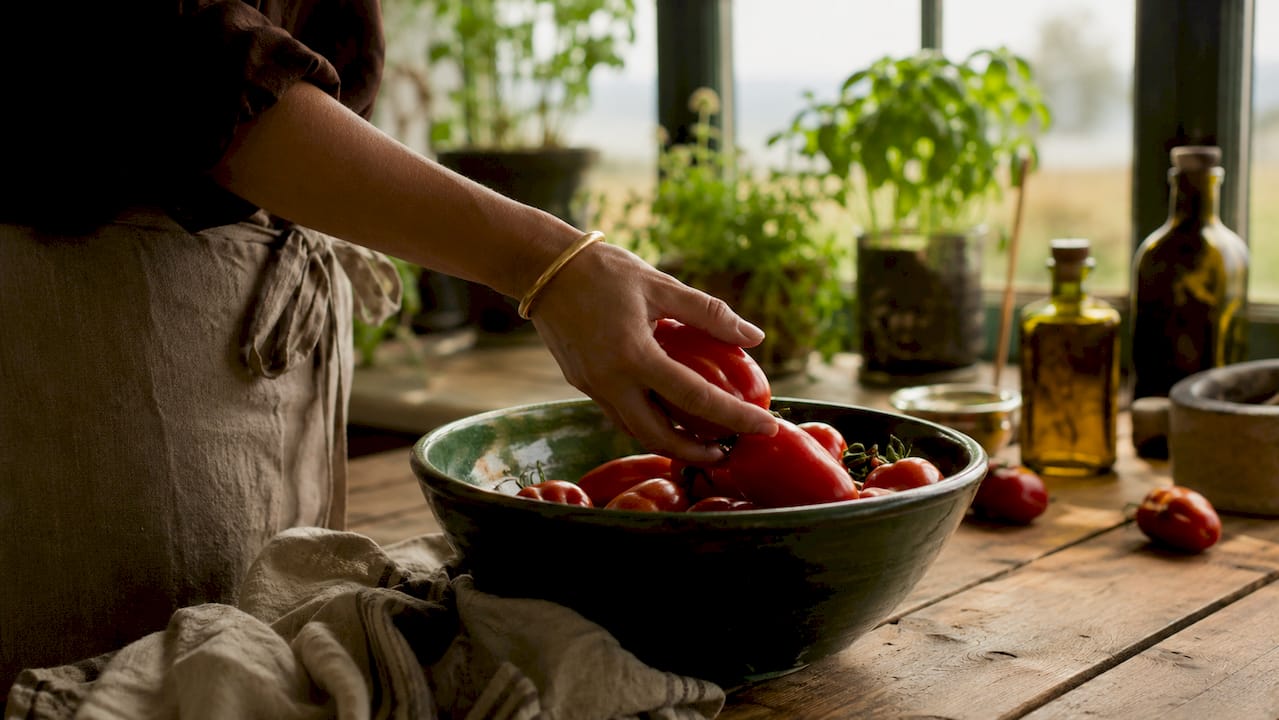 Eine Hand gibt San-Marzano-Tomaten in eine Pfanne in der Küche.