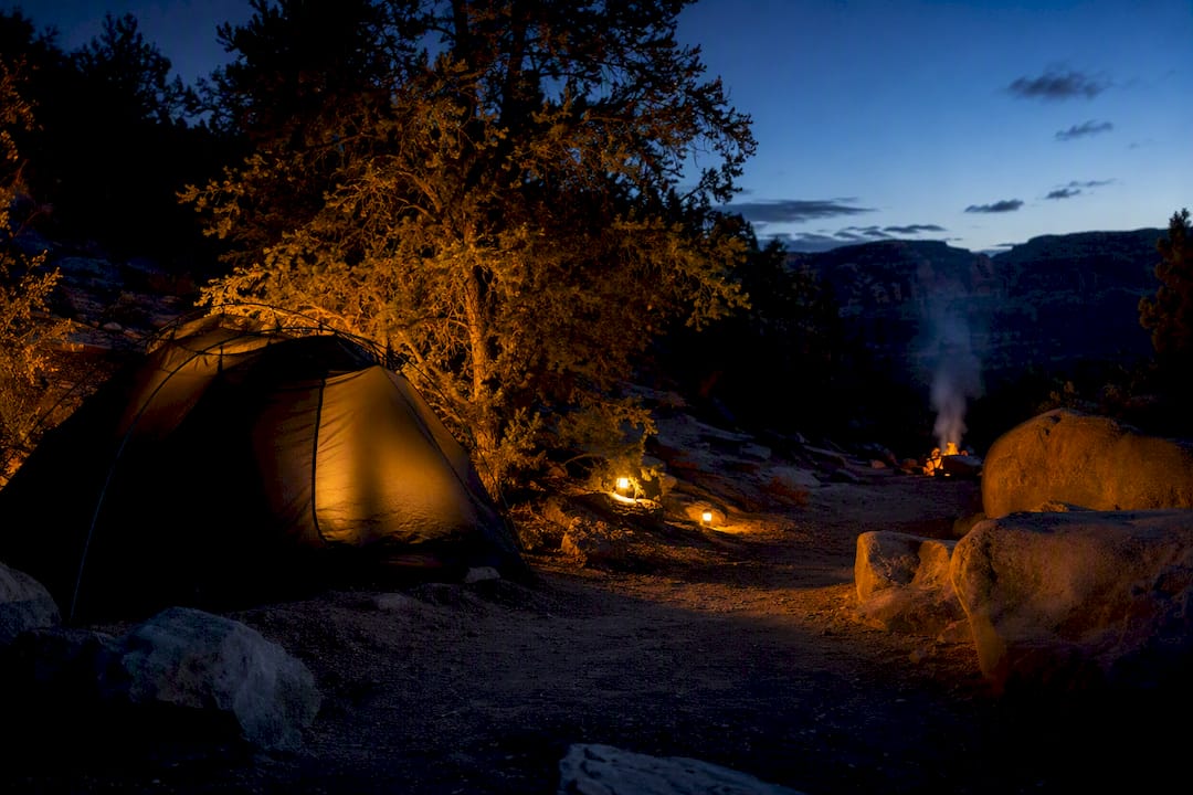 Amber-lit campsite zone with tent and rocks