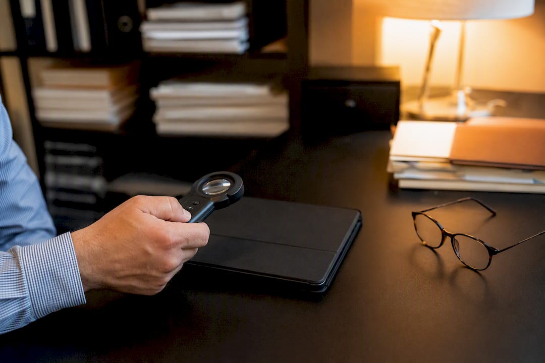 Close-up of hand with magnifier over tablet and glasses