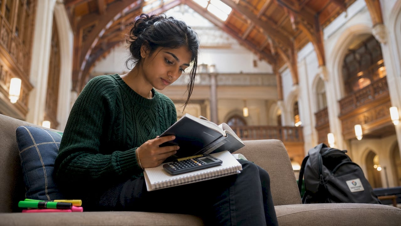 Female student studying engineering textbooks in library