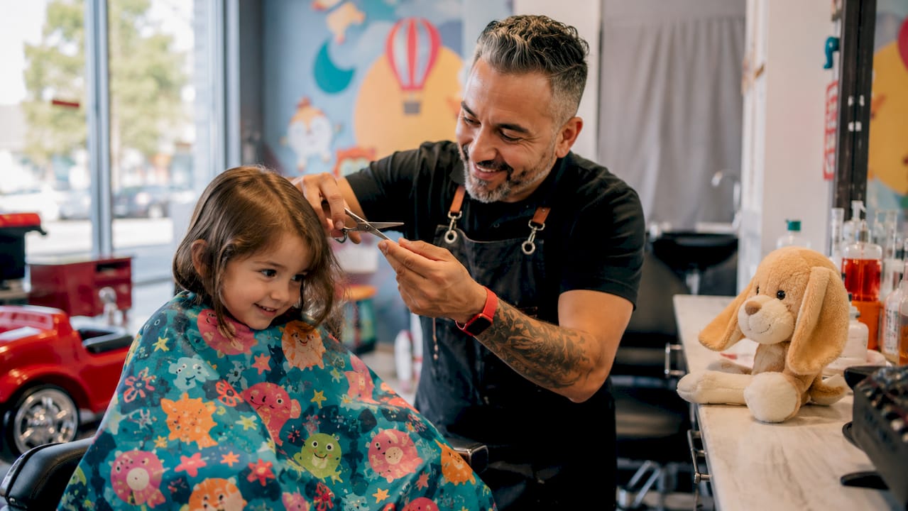 Side profile of patient barber trimming child’s hair