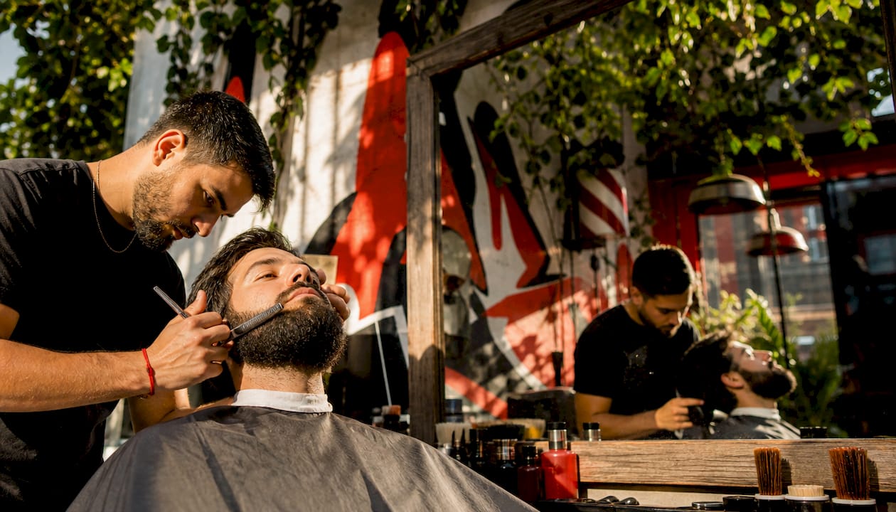 Barber shaping man's beard in modern barbershop