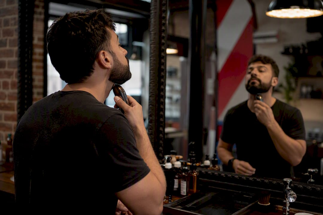 Man trimming beard neckline in bathroom mirror
