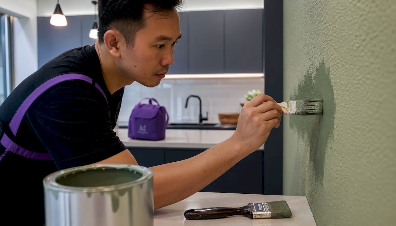Hands rolling muted green paint on small apartment wall
