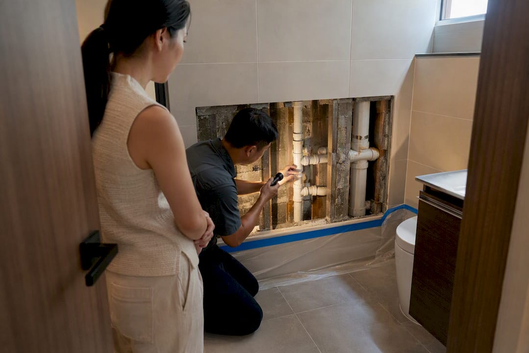 Asian homeowner viewing exposed bathroom plumbing