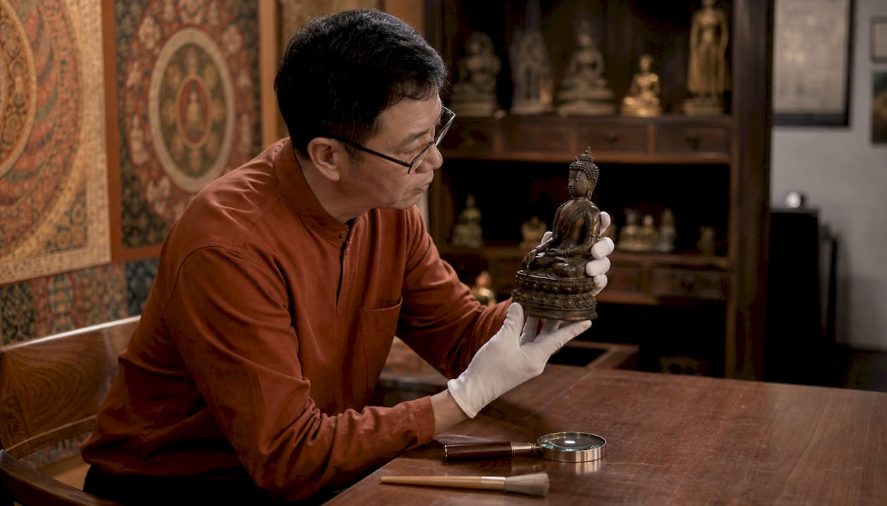 Curator examining bronze Buddha closely