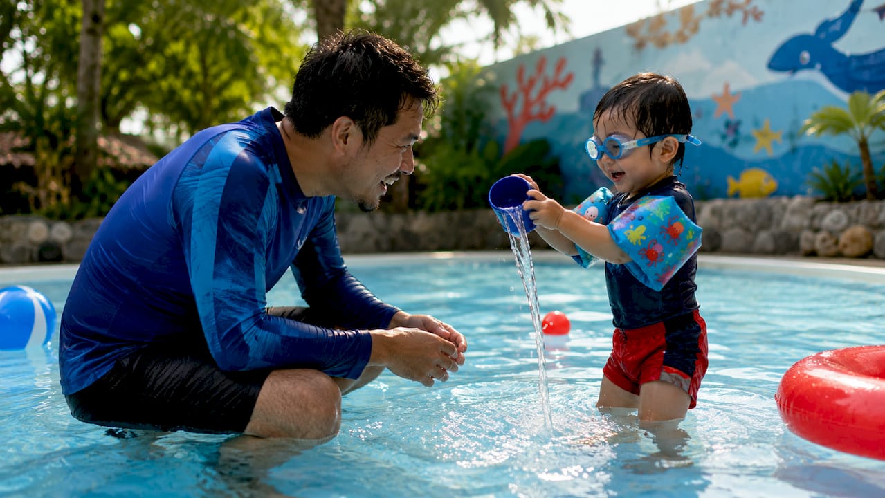 Mother encouraging toddler swim class at indoor pool