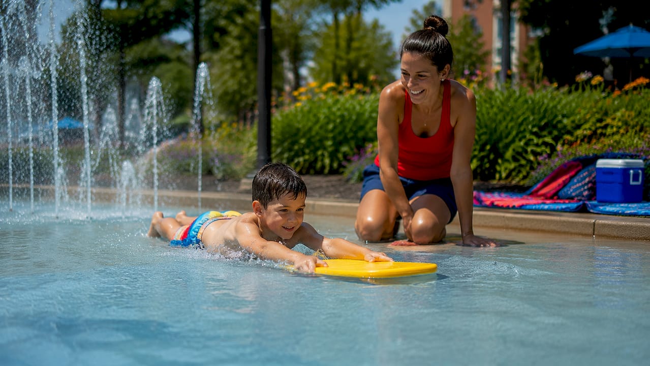 Mother supervising son using kickboard in home pool