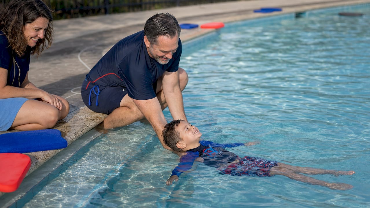 Swim instructor teaching young boy to float