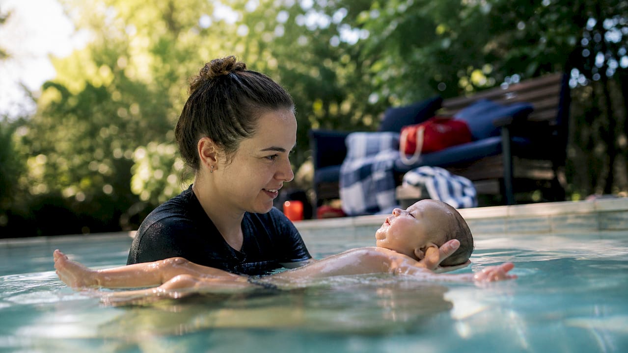 Parent supporting infant survival float in pool