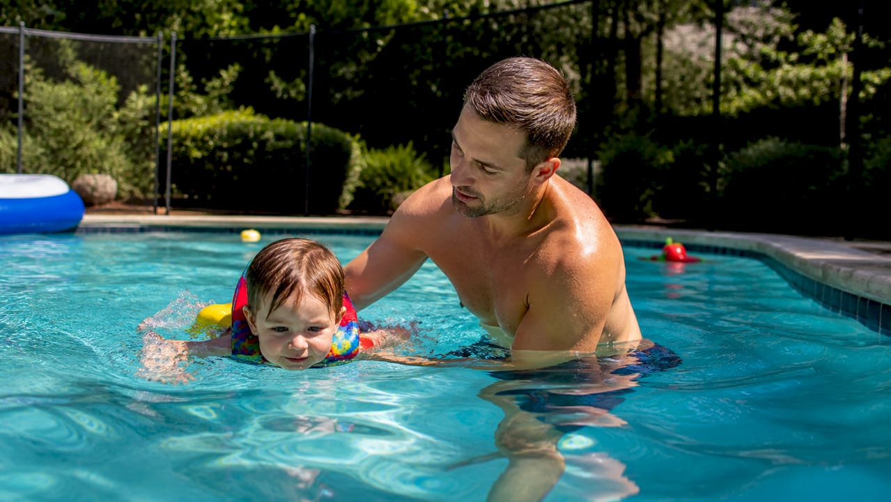 Adult supervising toddler swimming in life jacket