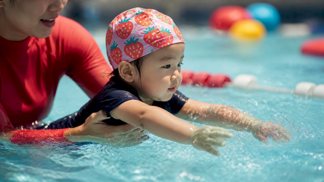Toddler practicing swim strokes with instructor support