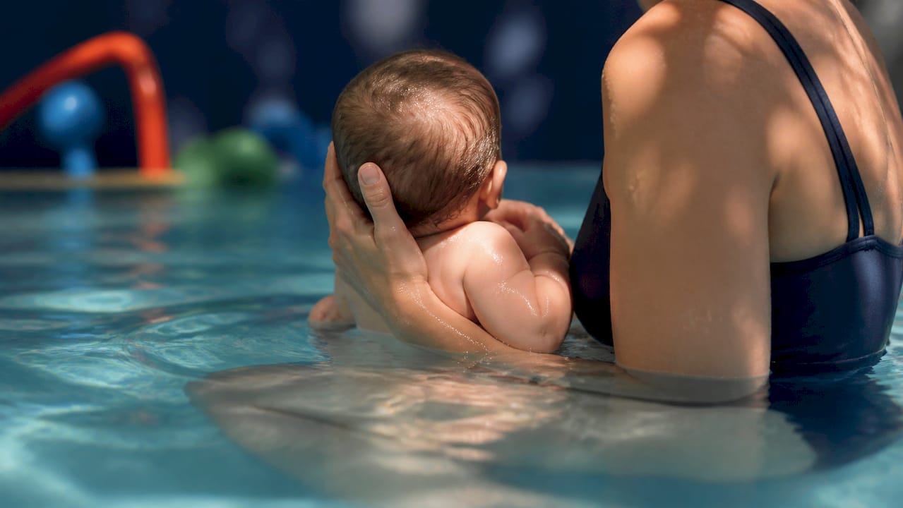 Parent holding infant upright in warm pool water