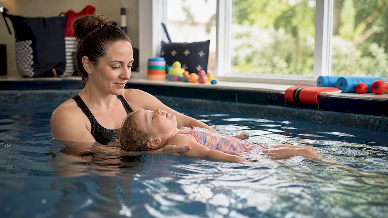 Swim instructor supporting toddler floating in pool