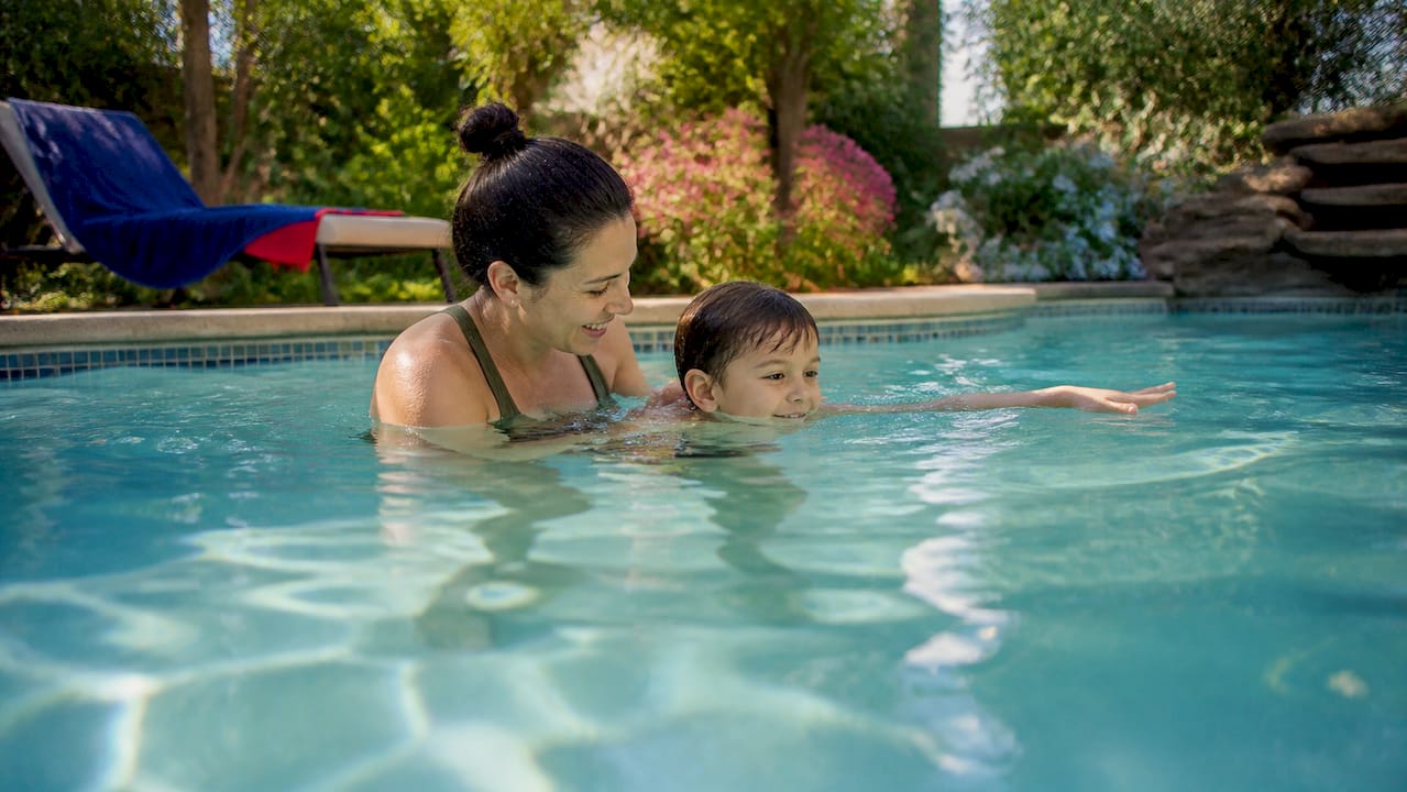Parent guiding child swimming at backyard pool